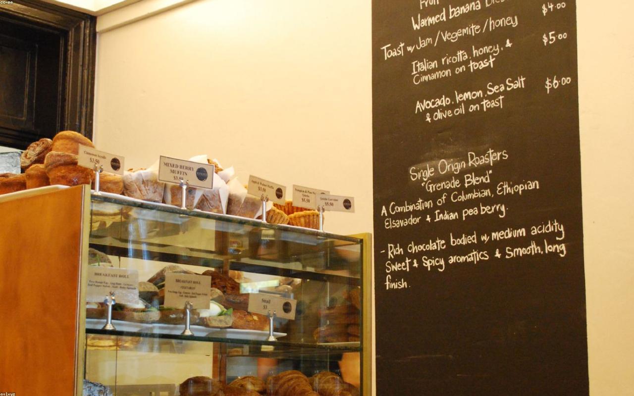 A bakery display case of breads and pastries, with a chalkboard menu behind the counter.